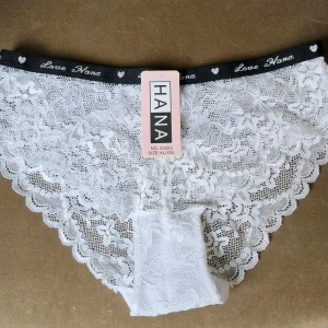 Vit spetsunderkläder från Love Hana - Säljer ett par eleganta vita spetsunderkläder från Love Hana. De har ett vackert blommönster och en elastisk midja med texten 'Love Hana' och små hjärtan. Perfekt för en romantisk touch i garderoben. Storlek 40