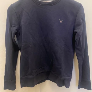 Mörkblå tröja från Gant - Säljer en stilren mörkblå tröja från Gant med rund halsringning och diskret logga på bröstet. Tröjan har långa ärmar och är perfekt för en avslappnad look. Passar barn i åldern 11-12 år.