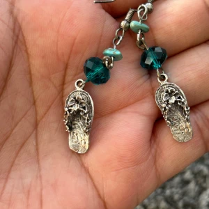Örhängen med turkosa pärlor och sandalmotiv - Unika örhängen med ett charmigt sandalmotiv i silverfärg. De har turkosa och mörkgröna pärlor som ger en bohemisk känsla. Perfekta för att lägga till en personlig touch till din stil.