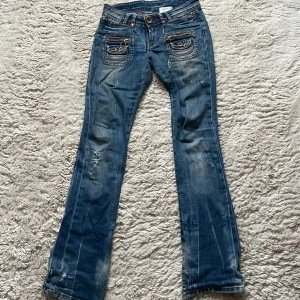 Blå jeans med detaljer - Snygga blå jeans med slitna detaljer och flera fickor med dragkedjor. De är utsvängda och i storlek 27/34.
