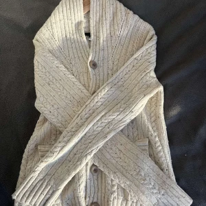 stickad kofta med knappar - Mysig beige stickad kofta med stora knappar och ribbad krage. Perfekt för kyliga dagar med sin klassiska design och bekväma passform. Koftan har två praktiska fickor framtill. Har du funderingar var inte rädd att kontakta oss!/ R.EsellingSWE😎