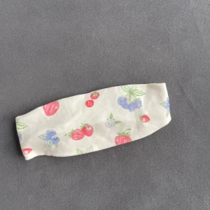 Mönstrat hårband från Djerf Avenue - Sött hårband från Djerf Avenue i bomull med ett fruktigt mönster i rött, blått och grönt på en vit bakgrund. 100% återvunnen bomull