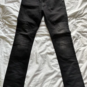 Nudie jeans - Snygga svarta jeansbyxor från nudie  med en slim fir  passform. Byxorna har en klassisk design med fem fickor och subtila slitningar för en trendig look. Perfekta för en stilren outfit.