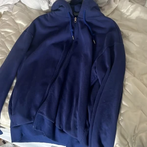 Mörkblå hoodie med dragkedja - Säljer en mörkblå hoodie med dragkedja och huva. Perfekt för en avslappnad stil. Den har långa ärmar och ribbade muddar vid ärmslut och nederkant.