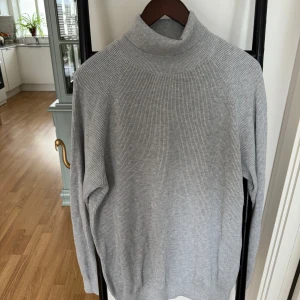 Grå polotröja från Dressmann - Säljer en stilren grå polotröja från Dressmann i ribbat material. Perfekt för kyligare dagar med sin höga krage och långa ärmar. Tröjan är i en neutral grå färg som passar till det mesta. Ett måste i garderoben för en klassisk look. Merinoull & bomull. Nypris 599kr