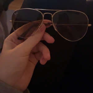 Solglasögon från Ray-Ban - Snygga Ray-Ban solglasögon med klassisk aviator-stil. De har en tunn guldfärgad metallram och mörka glas. Perfekta för en stilren look. Kommer med ett brunt fodral för säker förvaring.