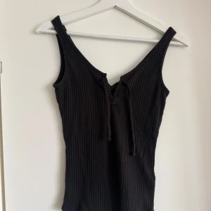 Svart ribbad linnetopp från Gina Tricot - Snygg svart ribbad linnetopp från Gina Tricot i storlek S. Toppen har en knytning framtill och är ärmlös, perfekt för en stilren look.