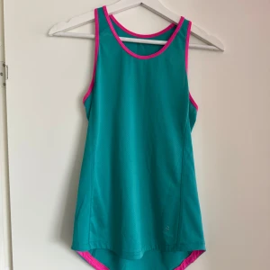Turkos linnetopp med rosa detaljer - Säljer en snygg turkos linnetopp med rosa kantdetaljer. Perfekt för träning eller en varm sommardag. Toppen har en sportig design med ärmlös stil och rund halsringning.