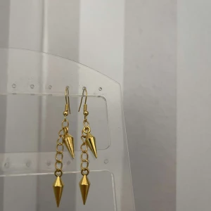 Guldörhängen med kedja och spetsig detalj - Snygga guldörhängen med en kedja och en spetsig, konformad detalj längst ner. Perfekta för att ge en edgy touch till din outfit. De är lätta och bekväma att bära hela dagen.