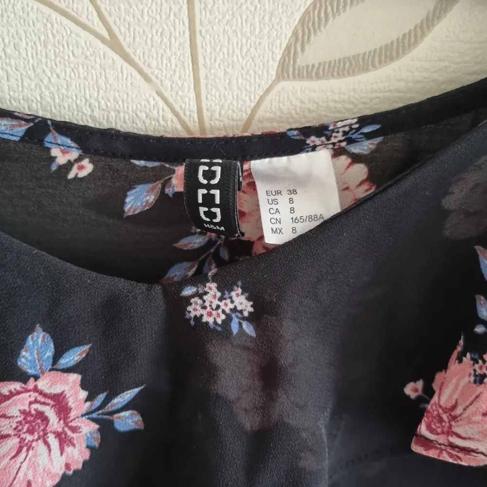 Säljer en superfin svart tunn blus från H&M i storlek 38 med rosa blommor och volangdetaljer. Toppen har korta ärmar och en söt offshoulder-stil med knytband på axlarna. Perfekt för sommarens fester eller en mysig vårdag!. Blusar.