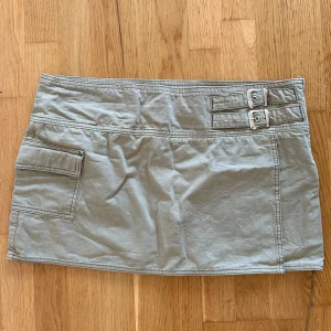 Olivgrön minikjol - Minikjol med spännedetalj och ficka samt overlap.