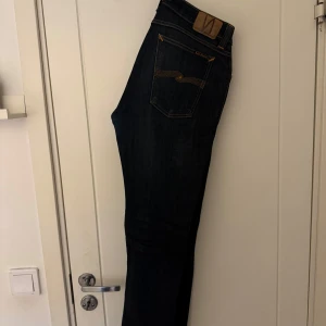 Mörkblå jeans från Nudie Jeans - Snygga mörkblå jeans från Nudie Jeans med klassisk femficksdesign och orange sömmar. Jeansen har en knappgylf och är tillverkade i ett slitstarkt denimtyg. Perfekta för en stilren look.Märke: Nudie Jeans Modell: Skinny Lin Storlek: 33/34 (obs uppsydda så längd är cirka ~30/31nu)  Färg: Blå  Nypris: ~1400kr  Inköpt för lite mer än 3 år sen. I bra skick.  Använt ett flertal gånger.  