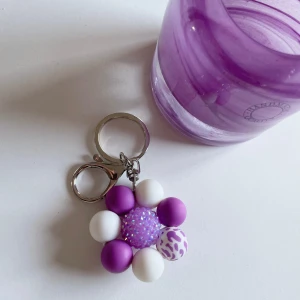 Handgjorda Nyckelring med silikon pärlor 🌸 -  Handgjord nyckelring i lila och vitt med pärlor i en blommig design. Stilren och lekfull accessoar som passar perfekt för att dekorera dina nycklar eller väskor. Unik och noggrant tillverkad🎀
