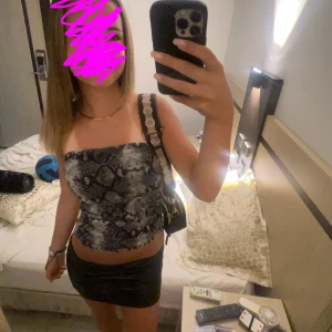 Ormskinnsmönstrad tubtopp - Snygg tubtopp med ormskinnsmönster i grå och svarta nyanser. Perfekt för en utekväll eller fest. Toppen är axelbandslös och har en tight passform. Storlek går också att justera med ett band under brösykrogen som ej syns eftersom den också är mönstrad. 