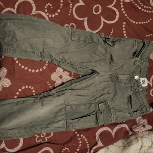 Grå cargopants med fickor - Säljer ett par grå cargopants med flera praktiska fickor. Byxorna har en avslappnad passform och är perfekta för en casual look. De är tillverkade i ett slitstarkt material och har en knapp- och dragkedjestängning.