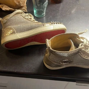 Guldiga christian louboutin  - Snygga glittriga sneakers i guld med nitar på tån och hälen. Skorna har snörning och en röd sula som ger en extra touch av stil. Perfekta för att sticka ut med en unik look. Skorna är från christian louboutin. De är väldigt unika och är limited edition!!❤️