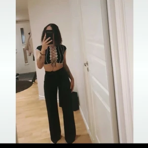 Svart croppad topp med snörning - Snygg svart croppad topp med vita detaljer och snörning framtill. Perfekt för en trendig look. Säljes oga jag har ej likadan tröja fast långärmad version 
