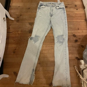 Ljusa jeans med slitningar från Zara - Säljer ett par ljusa jeans från Zara med slitningar på knäna och råa kanter. De har en straight passform och är högmidjade. Storlek M, normal i strl. Lite defekter så som smutsiga längst ned då dem vart för långa och blivit trampade på, det ha ej gått bort i tvätt men går evt om man försöker mer, eller syr upp/klipper av. En minimal fläck över knät också som ej syns på avstånd. 