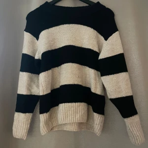 Randig tröja från Gina Tricot - Säljer en mysig randig tröja från Gina Tricot i svart och beige. Tröjan har långa ärmar och en bekväm passform, perfekt för kyligare dagar. Den är stickad och har breda ränder som ger en stilren look.