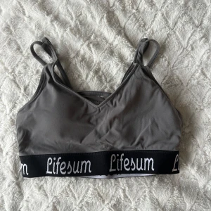 Sportbh Lifesum - Snygg grå sportbh från Lifesum med dubbla axelband och elastiskt band med logga under bysten. Storlek S/M. 