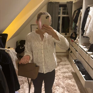 Vit blus från Vero Moda - Säljer en söt vit blus från Vero Moda med broderade detaljer och knappar framtill. Blusen har långa ärmar och en romantisk känsla, perfekt för vår och sommar.