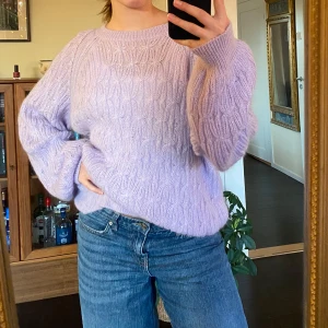 Ljuslila stickad tröja från Indiska  - Mysig ljuslila stickad tröja med ett fint kabelstickat mönster. Tröjan har långa ärmar och en rund halsringning, perfekt för kyligare dagar.