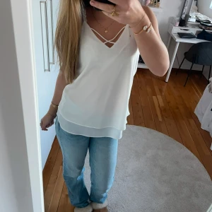 Vit ärmlös linnetopp - Snygg vit ärmlös linnetopp med dubbla axelband och v-ringad design. Perfekt för varma dagar och kan enkelt matchas med olika outfits.