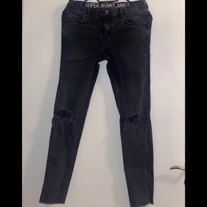 Svarta super skinny jeans - Snygga svarta super skinny jeans med slitna knän. Perfekta för en trendig look. De har en knapp och dragkedja framtill samt klassiska fem fickor.