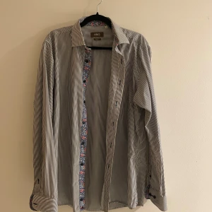 Randig skjorta från Ströms - Snygg randig skjorta från Ströms i slim fit. Skjortan har en diskret blommig detalj på insidan av kragen och knappslån. Perfekt för en stilren look.😉
