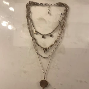 Flerlagrat halsband i silver - Snyggt flerlagrat halsband i silver med flera kedjor och små runda berlocker. Perfekt för att ge en stilfull touch till din outfit. Justerbar längd för bästa passform.