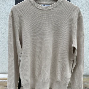 Beige stickad tröja från Zara - Säljer en stilren beige stickad tröja från Zara. Perfekt för kyligare dagar med sin mjuka och bekväma passform. Tröjan har långa ärmar och en klassisk rund halsringning. Ett måste i garderoben för en enkel och snygg look. Tröjan är använd 1-3 gånger så den är så gott som ny.