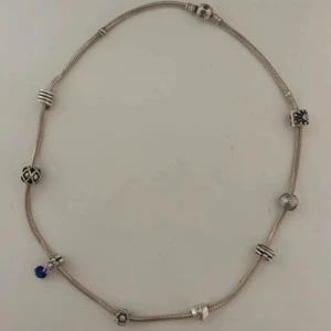 Silverfärgat halsband med berlocker från Pandora - Snyggt silverfärgat halsband från Pandora med flera unika berlocker. Själva halsbandet kostar 1500kr nypris och varje berlock kostar ca 350-800kr nypris! Så det är väldigt bra pris jag säljer för!🥰🥰 Armbandet har detaljer som en blå pärla och olika mönstrade berlocker som ger en personlig touch. Perfekt för att komplettera din stil med en elegant accessoar. 