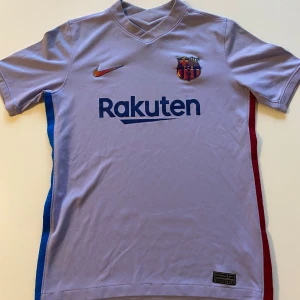 Lila FC Barcelona fotbollströja från Nike - Snygg FC Barcelona tredjetröja från säsongen 2021/22. Den är väldigt unik i stilen men är väldigt vacker. Storleken är 147-158 cm vilket mostsvarar storlek L i barn. Skick 8/10. Vid frågor och funderingar är det bara att kontakta mig!
