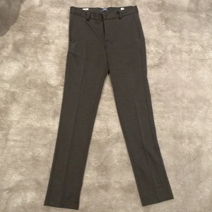 Grå kostymbyxor från Jack & Jones - Snygga grå kostymbyxor från Jack & Jones med en klassisk straight passform. Byxorna har hällor för bälte och knäppning fram. Perfekta för en stilren look.