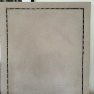 Beige sänggavel  - Elegant beige sänggavel med dekorativa nitar längs kanterna. Till för en 90 säng. Måtten är 90x100cm. Den har en mjuk och lyxig yta som ger ett stilrent intryck i sovrummet. Perfekt för att ge sängen en uppgradering och skapa en inbjudande atmosfär. Köpt från Frejas boning. Finns i Stockholm.