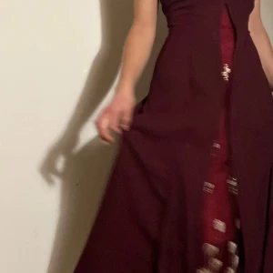 Balklänning - Elegant vinröd långklänning med vackra guldiga broderade detaljer. Funkar bra som balklänning eller vid andra speciella tillfällen. Går att knyta i ryggen