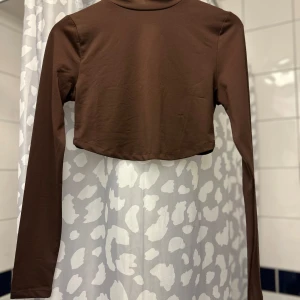 Brun croppad topp från NLY Trend - Säljer en brun croppad topp från NLY Trend. Toppen har långa ärmar och en enkel design som passar perfekt till olika outfits. Perfekt för en stilren look.