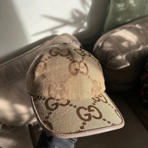 Beige keps med GG-mönster - Snygg beige keps med det ikoniska GG-mönstret. Perfekt för att ge din outfit en lyxig touch. Justerbar rem baktill för optimal passform.