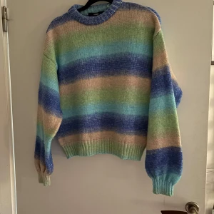 Randig stickad tröja från BikBok - Säljer en färgglad stickad tröja från BikBok i storlek S. Tröjan har ett randigt mönster i blått, grönt, beige och lila. Den är långärmad med ribbade muddar vid ärmslut och nederkant. Perfekt för en mysig dag!
