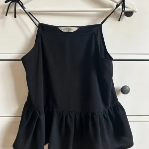 Svart linnetopp från H&M - Snygg svart linnetopp från H&M med smala axelband som knyts. Toppen har en volangdetalj vid nederkanten som ger en fin touch. Perfekt för varma dagar eller som en del av en lager-på-lager-look.