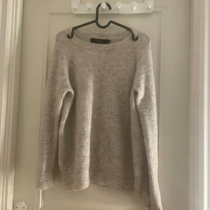 Beige stickad tröja från Vero Moda - Mysig beige stickad tröja från Vero Moda i storlek XS. Tröjan har långa ärmar och dekorativa knappar på sidan. Perfekt för kyliga dagar!