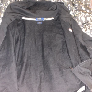 Svart huvtröja från Polo Ralph Lauren - Säljer en svart huvtröja från Polo Ralph Lauren med röd broderad logotyp på bröstet. Tröjan har dragkedja och långa ärmar, perfekt för en casual look. Den är riktigt skön och najs men är lite liten i storlek L så typ medium/ large. Bra sick inget defekt eller nåt liknade. Köpte fel storlek och den har gått ut och kan inte lämna tillbaka. 