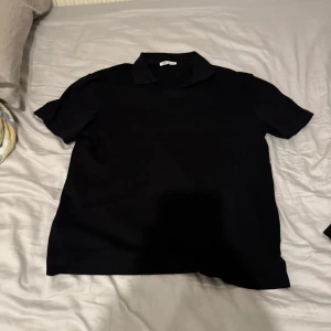 Svart kortärmad t-shirt med krage från Zara - Snygg svart t-shirt med krage och korta ärmar. Perfekt för en stilren look. 