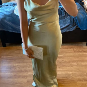 Ljusgrön / champangefärgad sidenklänning / satinklänning, balklänning  - Elegant ljusgrön/champange långklänning i siden med smala axelband och öppen rygg. Klänningen har en v-ringad design och knytning i ryggen för en stilren look. Perfekt för speciella tillfällen.