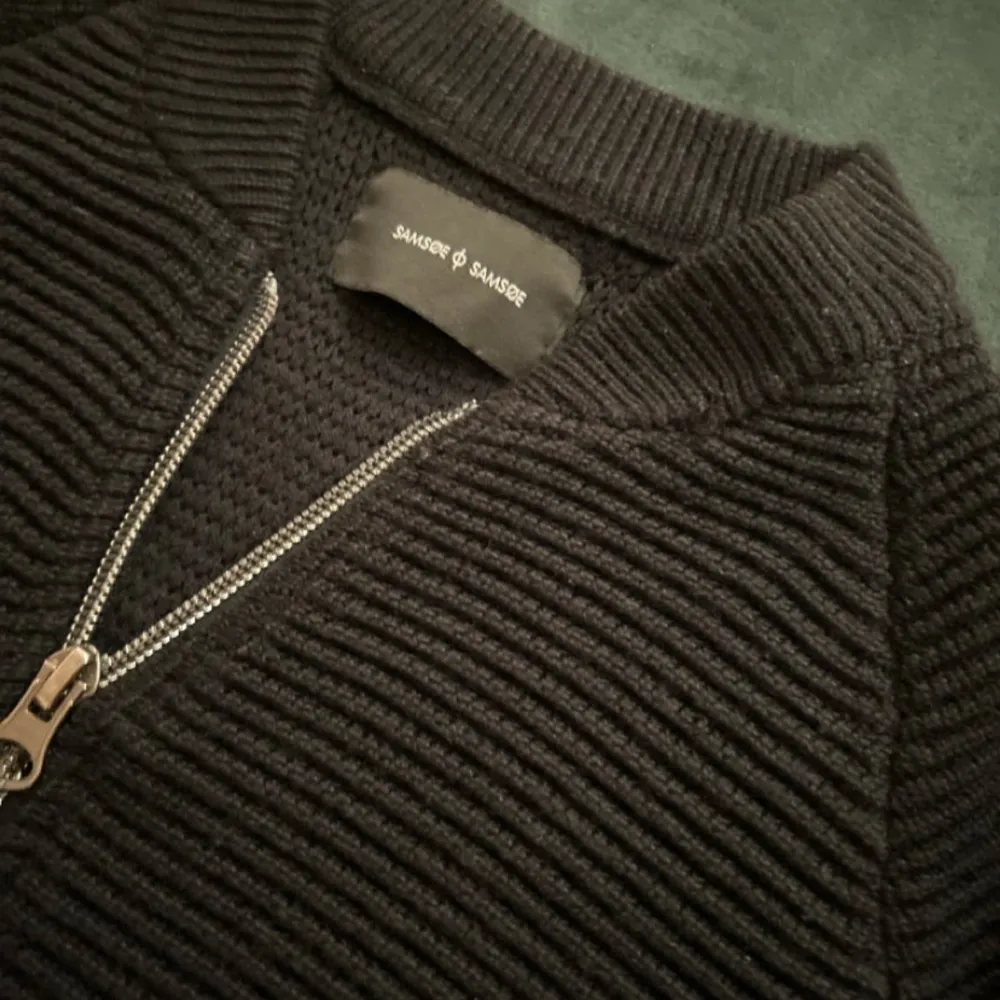 En stilren och mångsidig stickad full zip, tillverkad i en mörk, ribbad textur som ger en modern look. Med en hög kvalitet och enkel design är den perfekt för både vardagsbruk och mer uppklädda tillfällen. Nypriset ligger på cirka 1500 kr.⚡️. Neuletakit & Villapaidat.