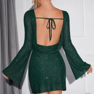 Glittrig grön klänning från Parthea  - Glittrig grön klänning från Parthea med öppen rygg och knytband. Klänningen har långa ärmar och en figurnära passform. Klänningen är i storlek XS, nyskick och aldrig använd. Org pris: 539kr. Nypris 279kr