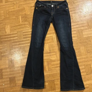 Mörkblå bootcut jeans från True Religion - Säljer mina favorit byxor då de tyvärr är för små! De har repats upp lite längst ner på vänstra benet men det är enda defekten. Innerbenslängden är 81cm, rakt över midjan är 37cm och benöppningen är 26cm. Skriv gärna innan köp. 