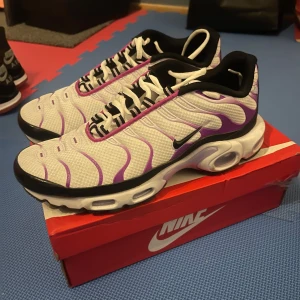 Nike sneakers i vitt och lila - Säljer ett par snygga Nike sneakers i vitt med lila och svarta detaljer. De har en cool design med vågiga linjer och en bekväm sula. Perfekta för både vardag och träning. Skorna är i nyskick och kommer i originalkartong.