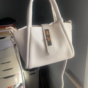 Vit handväska med gulddetaljer - Säljer en superfin vit handväska i syntetmaterial. Den har en stilren design med gulddetaljer och en praktisk dragkedja. Perfekt för både vardag och fest! 💖