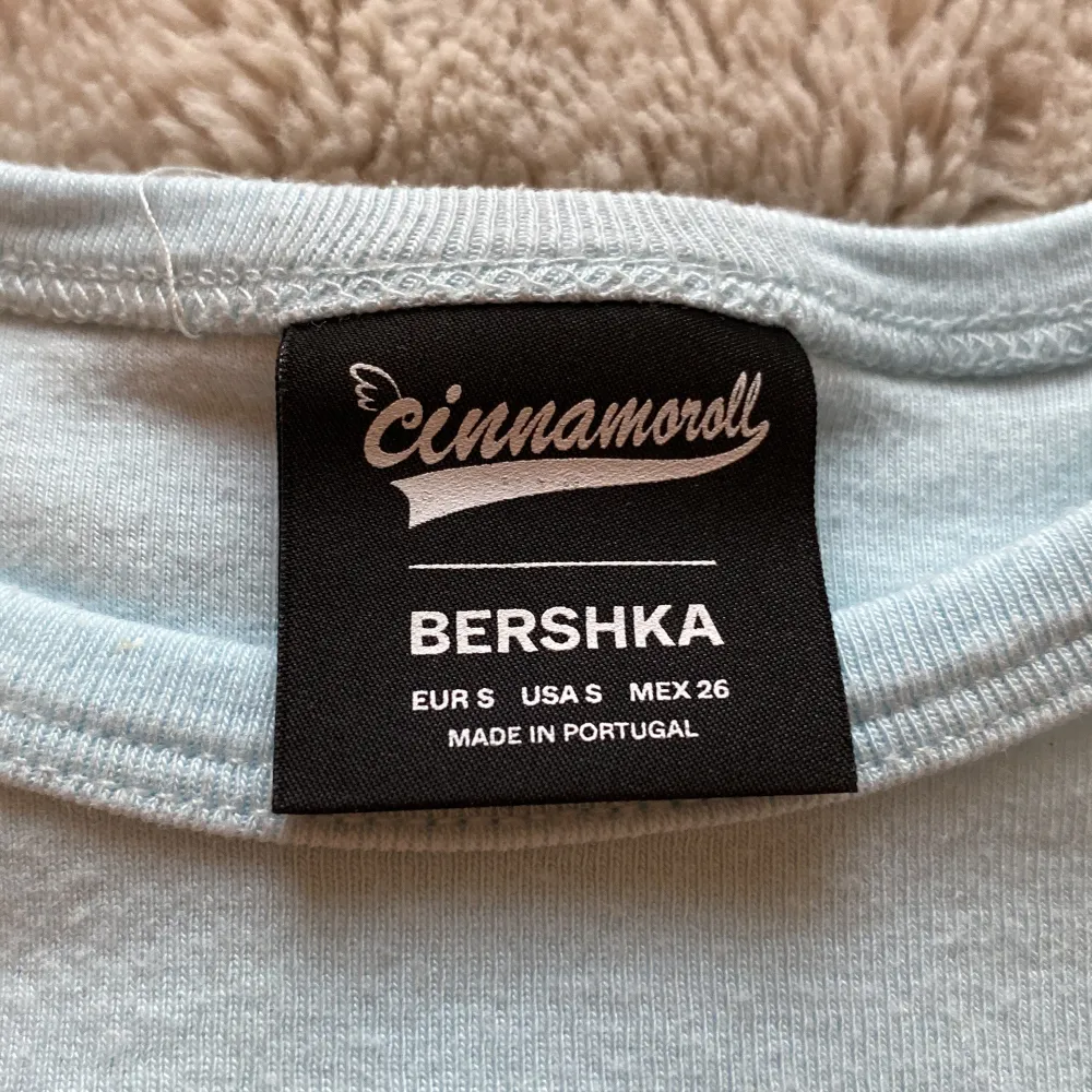 Supergullig ljusblå t-shirt från Bershka med Cinnamoroll-tryck på framsidan. Den har korta ärmar och är perfekt för en avslappnad stil. Texten 'warm heart and wagging tail' ger en extra söt touch. Perfekt för alla Cinnamoroll-fans!💙🩵. T-shirts.